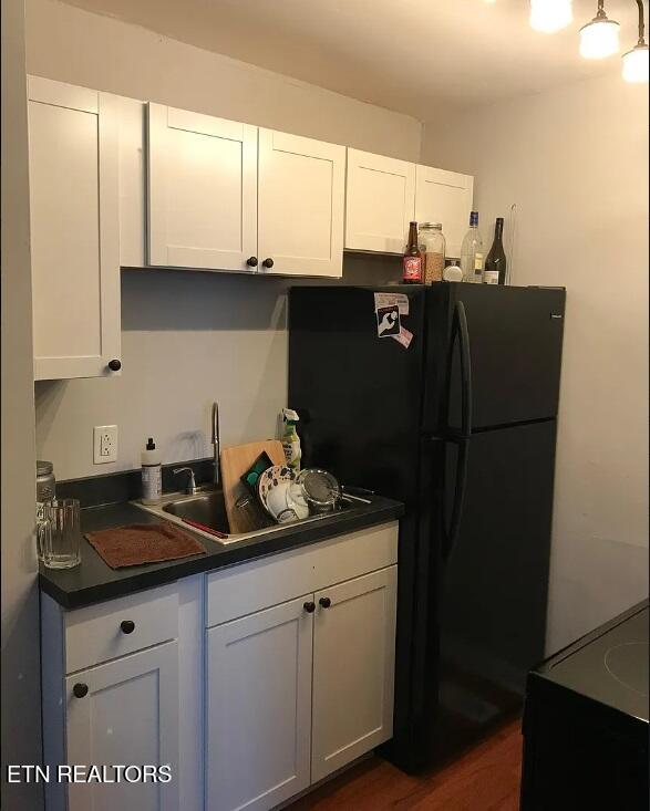kitchen with freestanding refrigerator, a sink, dark countertops, and white cabinetry