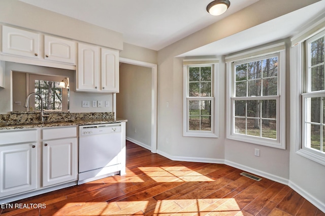 kitchen with stone counters, visible vents, a sink, dishwasher, and baseboards