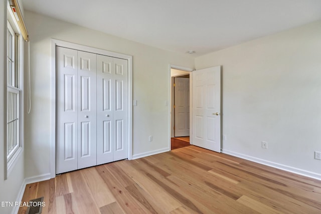 unfurnished bedroom with a closet, light wood-style flooring, and baseboards