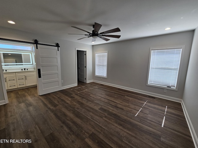 unfurnished bedroom featuring multiple windows, a barn door, dark wood-type flooring, and baseboards