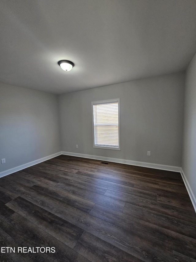 spare room featuring visible vents, baseboards, and dark wood-type flooring