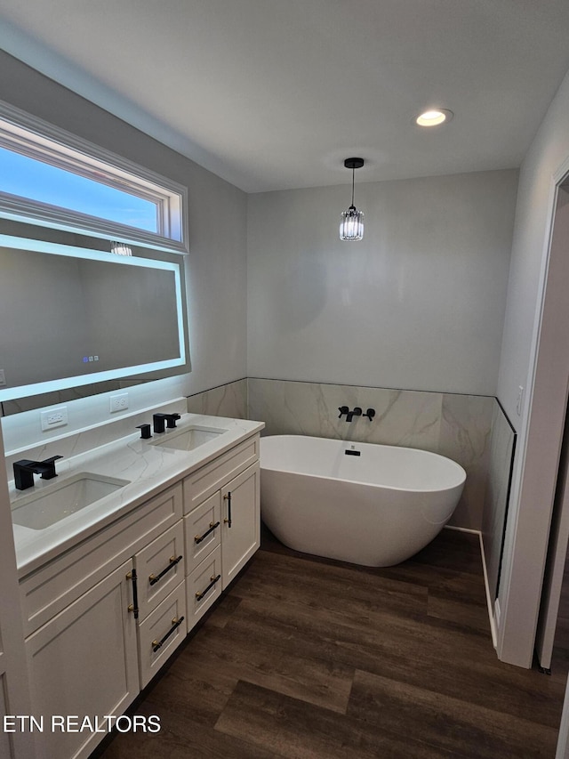 bathroom with double vanity, a freestanding bath, a sink, and wood finished floors