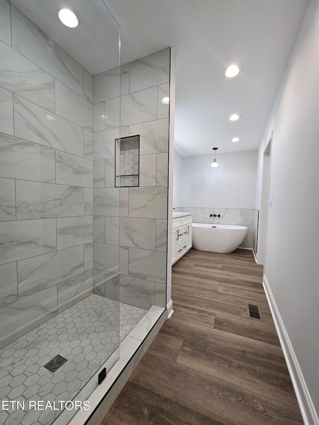 bathroom featuring a soaking tub, visible vents, wood finished floors, tiled shower, and baseboards