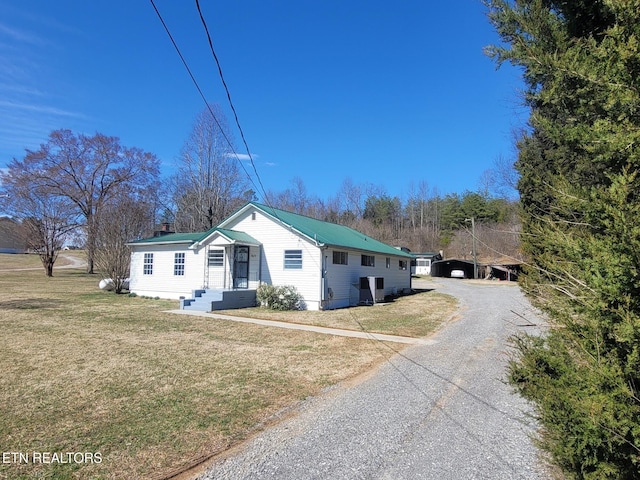 view of front facade featuring driveway, metal roof, and a front yard