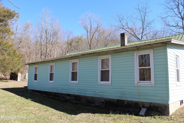 view of side of home with metal roof, a chimney, and a lawn