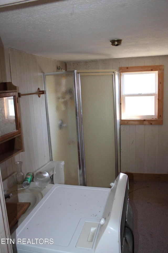 full bath with wood walls, a shower stall, washer / clothes dryer, and a textured ceiling