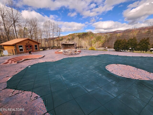 view of swimming pool featuring a view of trees, a patio, a fenced backyard, an outbuilding, and an exterior structure