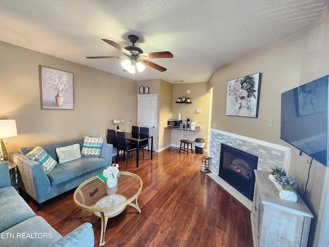 living room featuring a textured ceiling, a fireplace with flush hearth, wood finished floors, a ceiling fan, and baseboards