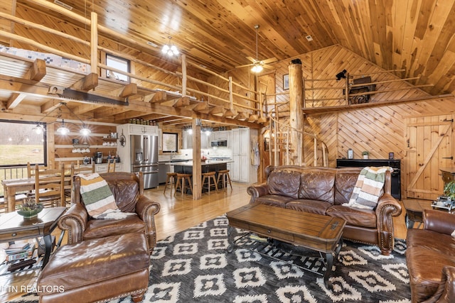 living area with light wood-style floors, a ceiling fan, wood ceiling, wood walls, and high vaulted ceiling