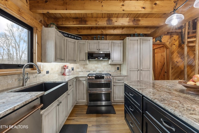 kitchen featuring beam ceiling, light wood finished floors, stainless steel appliances, decorative backsplash, and a sink