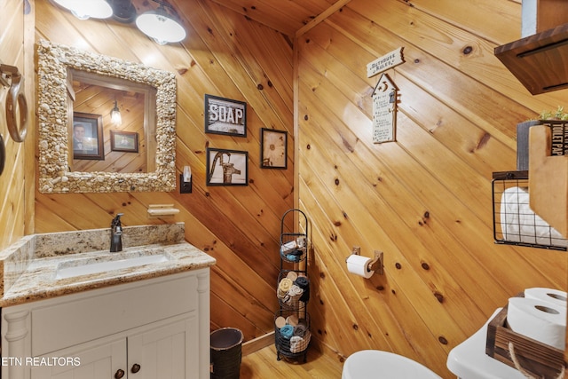 bathroom featuring toilet, wooden walls, and vanity