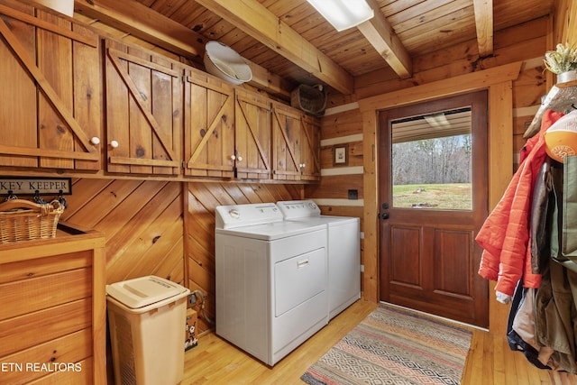 laundry area featuring light wood finished floors, wood walls, washer and clothes dryer, and cabinet space