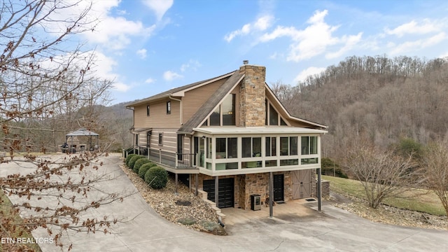 rear view of house with driveway, a chimney, stone siding, and a sunroom