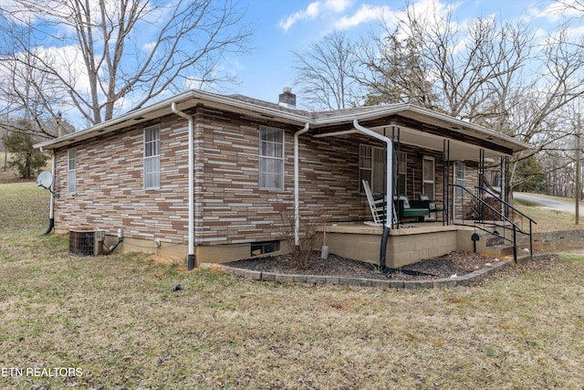 view of side of home with stone siding, a chimney, covered porch, a yard, and central air condition unit