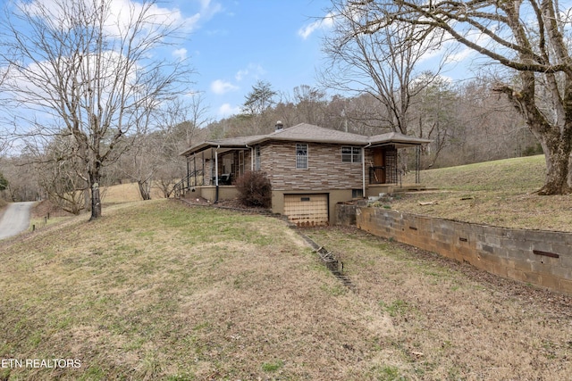 rear view of property featuring a yard, a chimney, dirt driveway, an attached garage, and stone siding