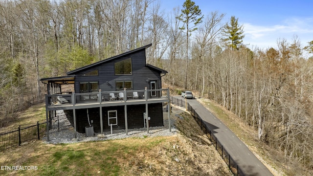 rear view of property featuring fence, a deck, a forest view, and central AC unit