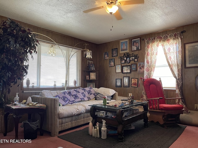 living room featuring wooden walls, carpet, a textured ceiling, and a ceiling fan