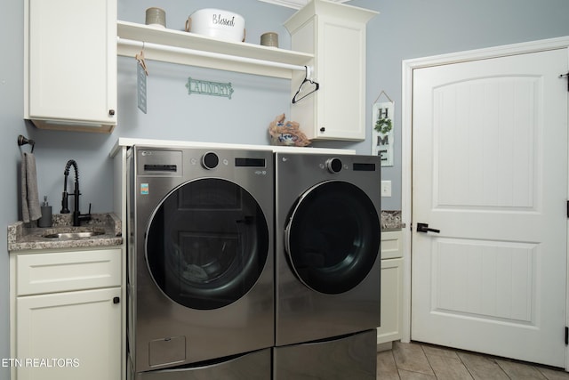 clothes washing area with cabinet space, a sink, and washing machine and clothes dryer