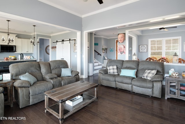 living area with ceiling fan with notable chandelier, a barn door, and dark wood-style floors