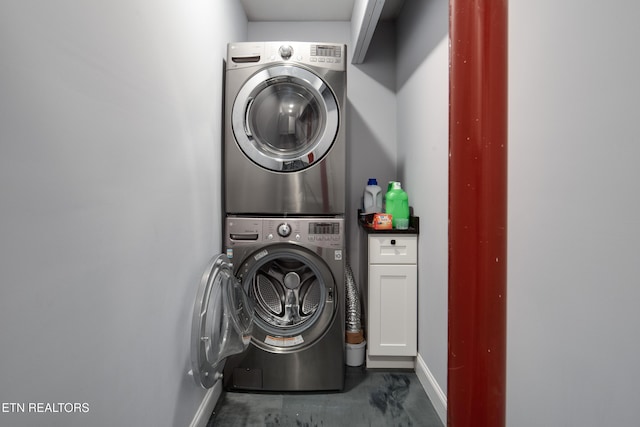 clothes washing area featuring stacked washing maching and dryer, baseboards, and cabinet space