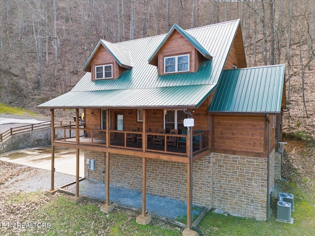 exterior space featuring central air condition unit, a forest view, and metal roof