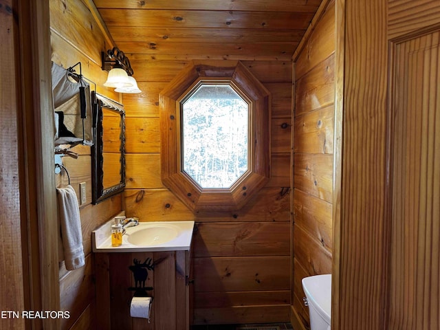 half bathroom featuring wood ceiling, vanity, toilet, and wooden walls