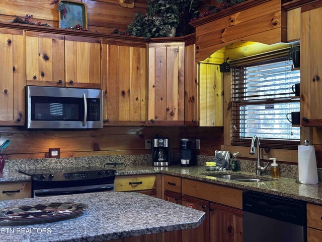 kitchen with brown cabinets, dark stone counters, stainless steel appliances, and a sink