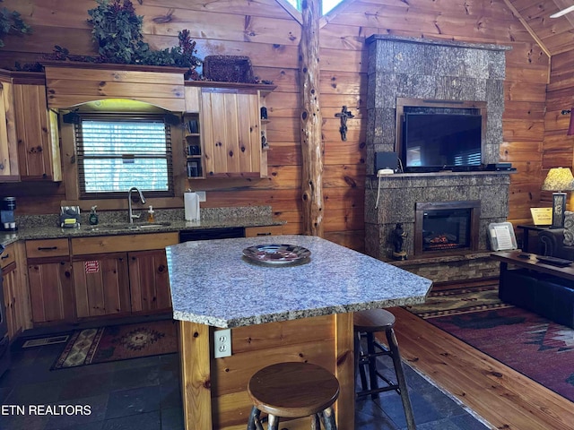 kitchen featuring lofted ceiling, wooden walls, a sink, and a stone fireplace