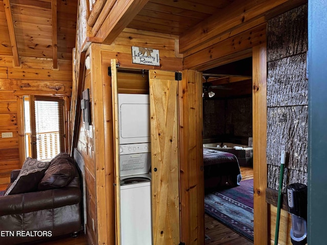 interior space with beam ceiling, stacked washer / drying machine, wood ceiling, wood walls, and wood finished floors