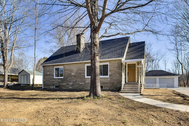 view of front of property with a detached garage, roof with shingles, a chimney, an outbuilding, and stone siding