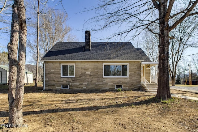 back of house featuring stone siding, roof with shingles, and a chimney