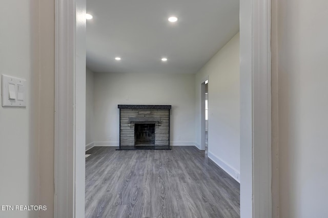 unfurnished living room with recessed lighting, baseboards, a stone fireplace, and wood finished floors