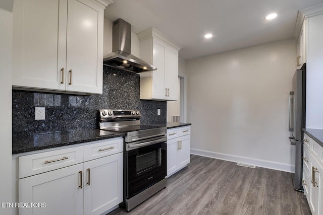 kitchen featuring wood finished floors, appliances with stainless steel finishes, white cabinetry, wall chimney exhaust hood, and backsplash