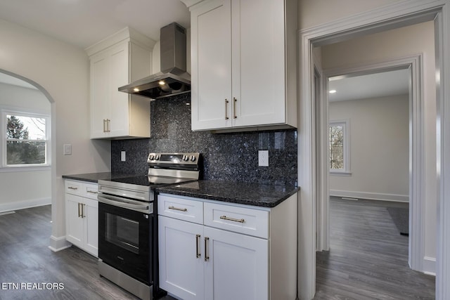 kitchen with backsplash, stainless steel electric stove, arched walkways, wall chimney exhaust hood, and white cabinets