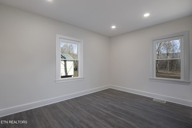 empty room featuring dark wood finished floors, visible vents, and baseboards