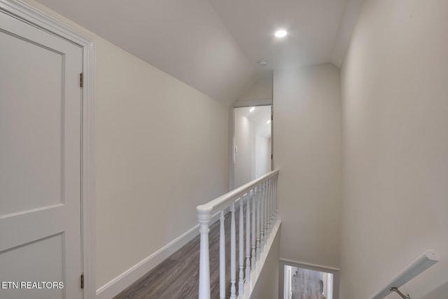 hallway featuring baseboards, an upstairs landing, lofted ceiling, and wood finished floors