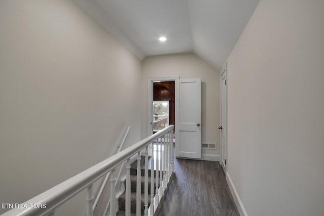 hall with visible vents, baseboards, dark wood-style flooring, vaulted ceiling, and an upstairs landing