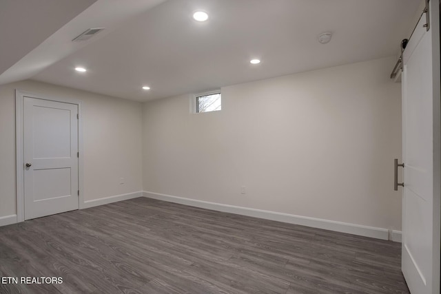 below grade area with visible vents, baseboards, dark wood finished floors, a barn door, and recessed lighting