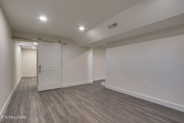 below grade area featuring a barn door, baseboards, visible vents, and wood finished floors