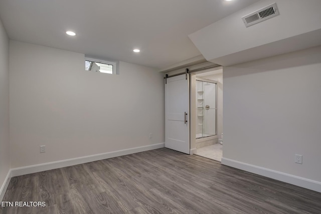 basement with visible vents, a barn door, baseboards, and wood finished floors