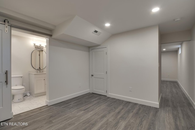 basement featuring a barn door, baseboards, dark wood-type flooring, and visible vents