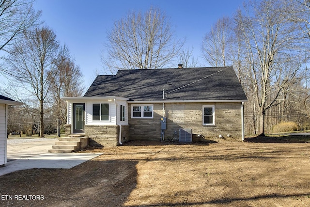 back of house featuring central air condition unit, stone siding, and roof with shingles