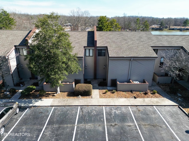 exterior space featuring a water view, uncovered parking, and roof with shingles