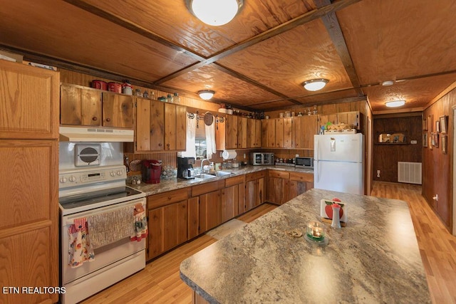 kitchen with wooden walls, under cabinet range hood, white appliances, a sink, and visible vents