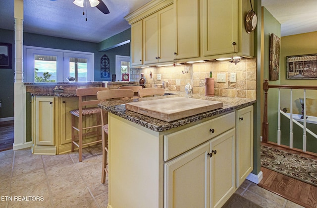 954 Pawnee Ct, Sevierville, TN 37876 - kitchen with cream cabinets, a breakfast bar, dark stone counters, ceiling fan, and decorative backsplash