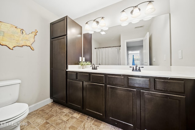 full bathroom featuring double vanity, a sink, toilet, and baseboards