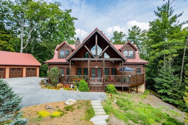 view of front facade featuring a garage, a chimney, metal roof, and an outbuilding