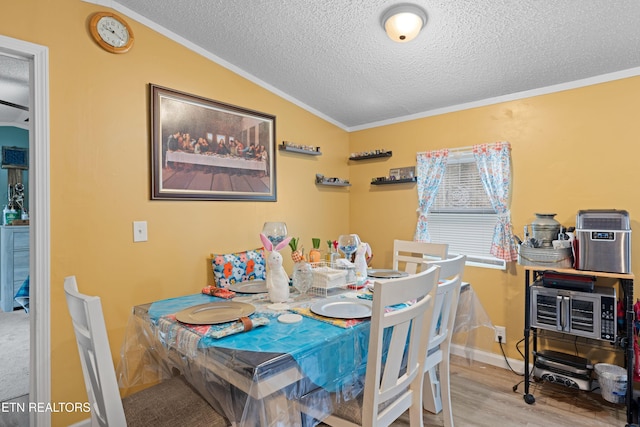 dining area with a textured ceiling, wood finished floors, baseboards, vaulted ceiling, and crown molding