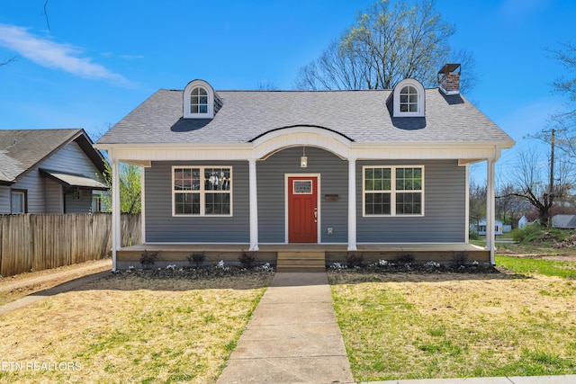 view of front facade featuring covered porch, roof with shingles, a chimney, fence, and a front lawn