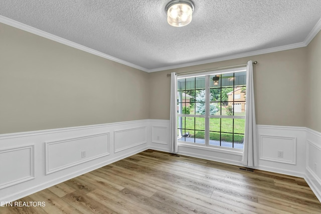 spare room featuring a wainscoted wall, a textured ceiling, visible vents, and wood finished floors